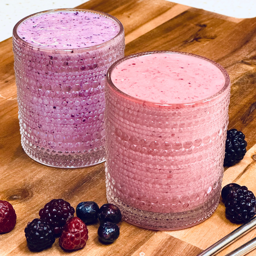 Two smoothies on counter with fruit and straws